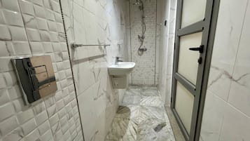 Ein Badezimmer mit weißen Marmorfliesen, einer Dusche, einem Waschbecken und einer Toilette.
