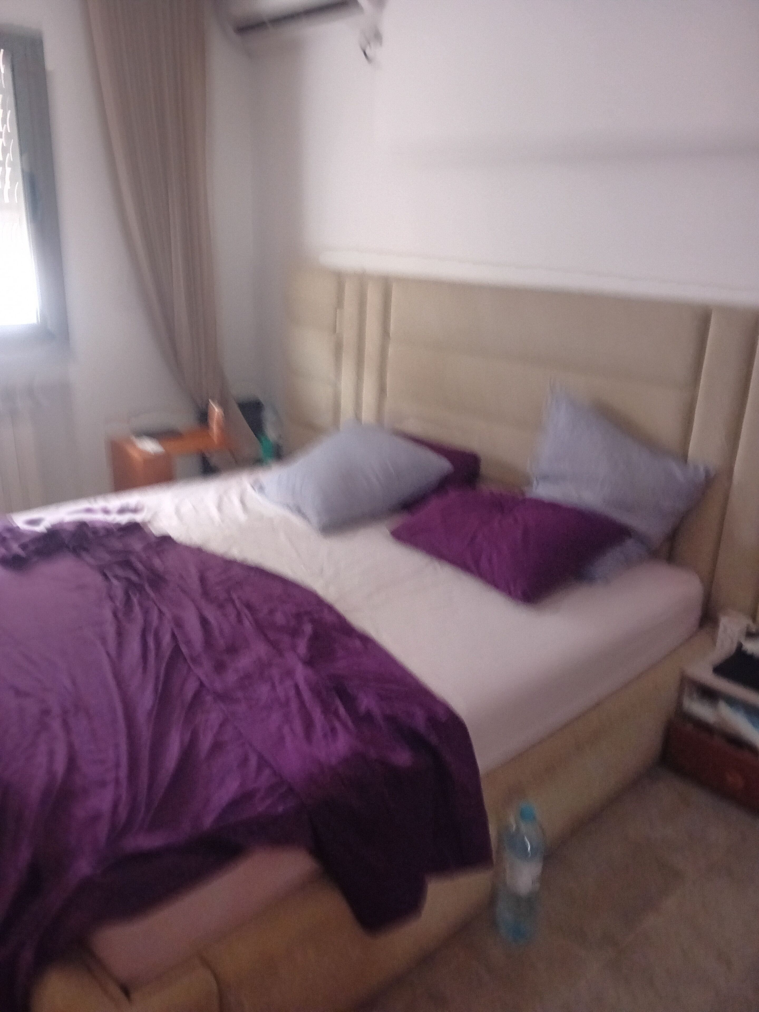 A bed with a headboard, a purple blanket, and two pillows.