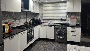 Una cocina moderna con gabinetes blancos, horno empotrado, microondas, lavadora y un lavamanos.