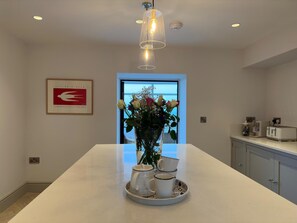 Una cocina moderna con una isla central, una obra de arte enmarcada, un florero y vistas a través de la puerta.