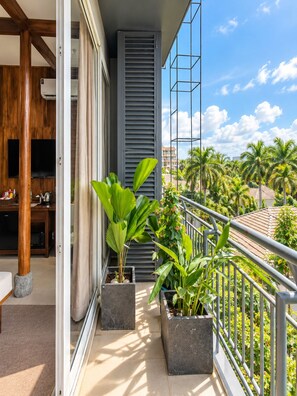 A balcony with potted plants, a TV, and a view of palm trees. - Nexus House Lang Bao Chi (Ho Chi Minh City)