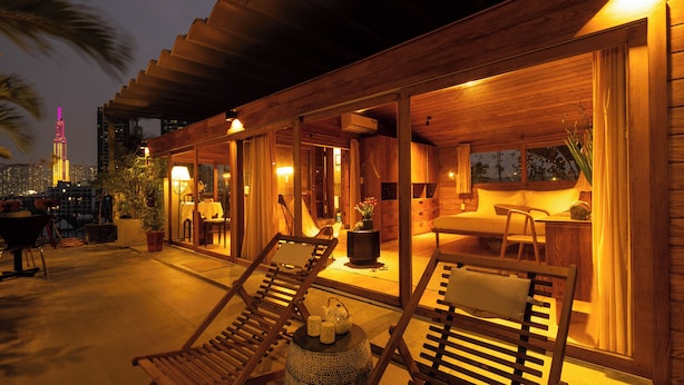 Una villa de madera con un patio que cuenta con sillones de descanso y una mesa de comedor.