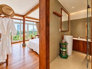 A hotel room with a bed, a bathroom with a sink and mirror, and a view of the city. - Nexus House Lang Bao Chi (Ho Chi Minh City)