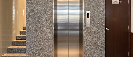 A modern elevator with a metallic finish, a digital control panel, and a wooden door with a sign indicating a toilet.