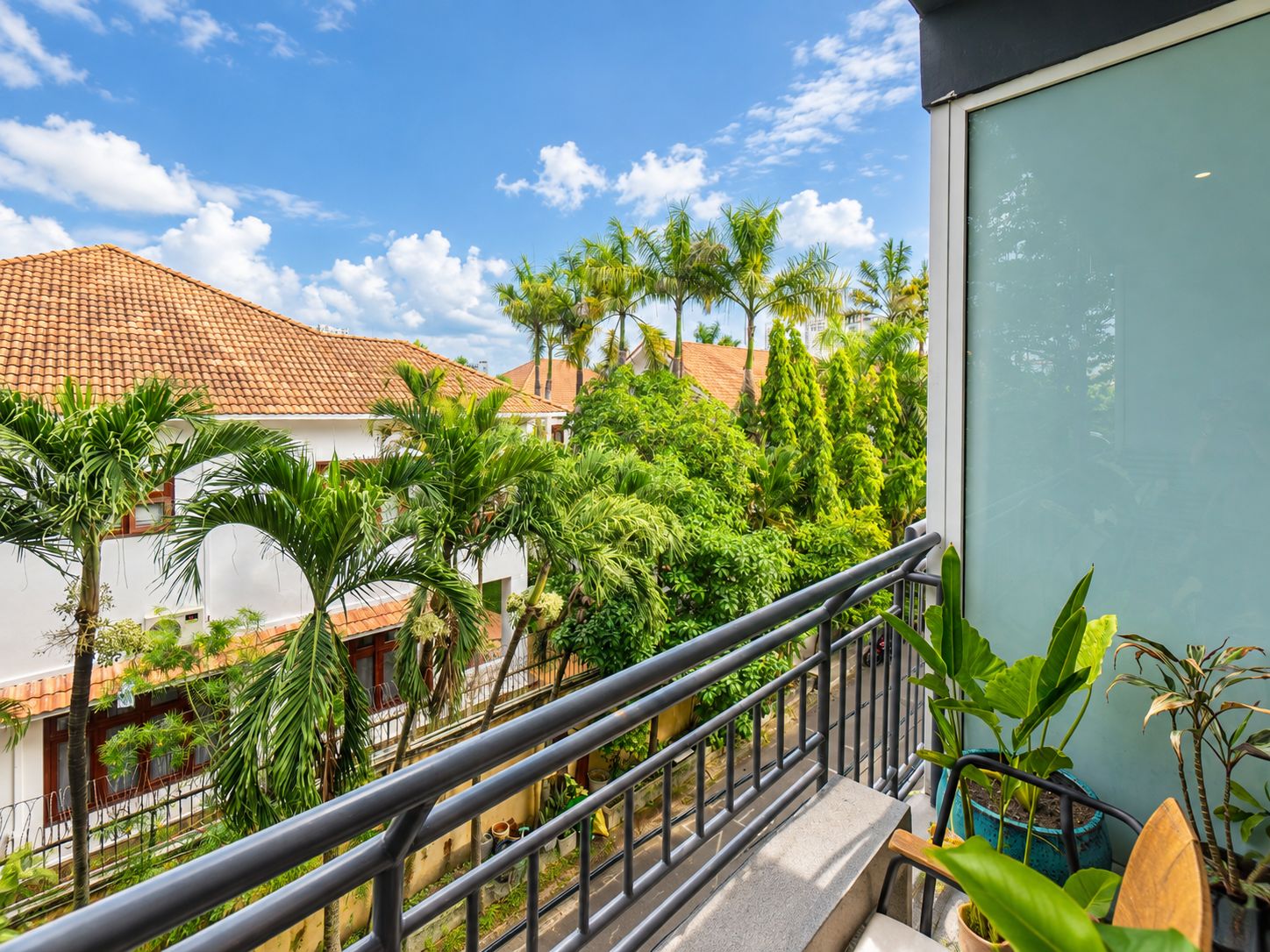 A balcony with a metal railing overlooking a residential area with houses and lush greenery.