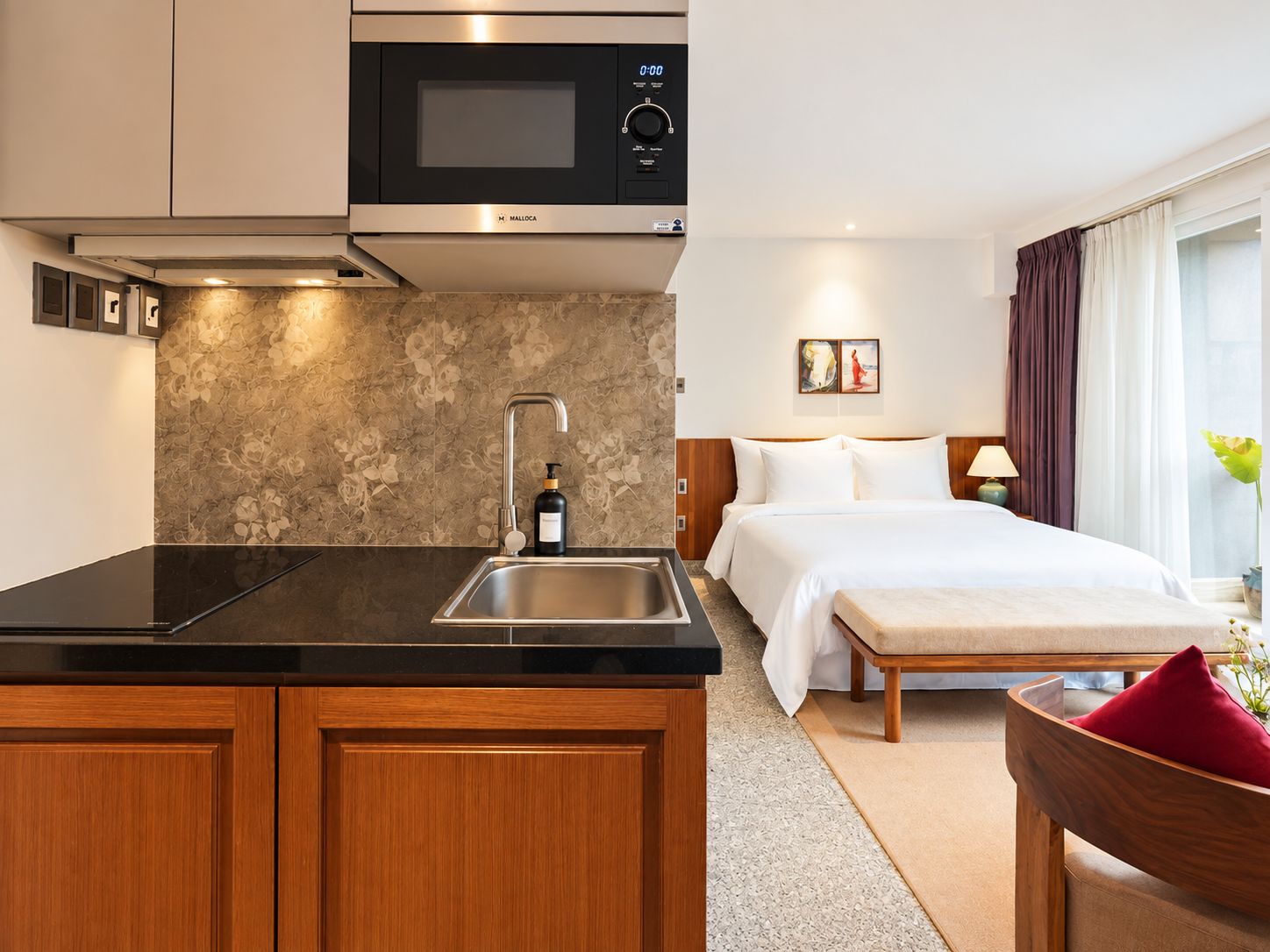 Ein modernes Hotelzimmer mit Küchenzeile, einem Bett, einem Nachttisch und einem Vorhangfenster.