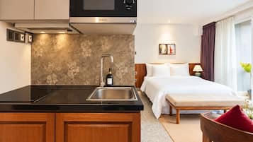 Una habitación de hotel moderna con kitchenette, una cama, una mesita de noche y un ventanal con cortinas.