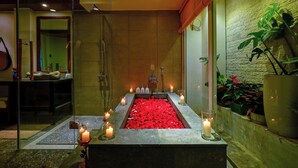 Zona de spa con un jacuzzi rodeado de velas, una pared de vidrio y plantas en macetas.