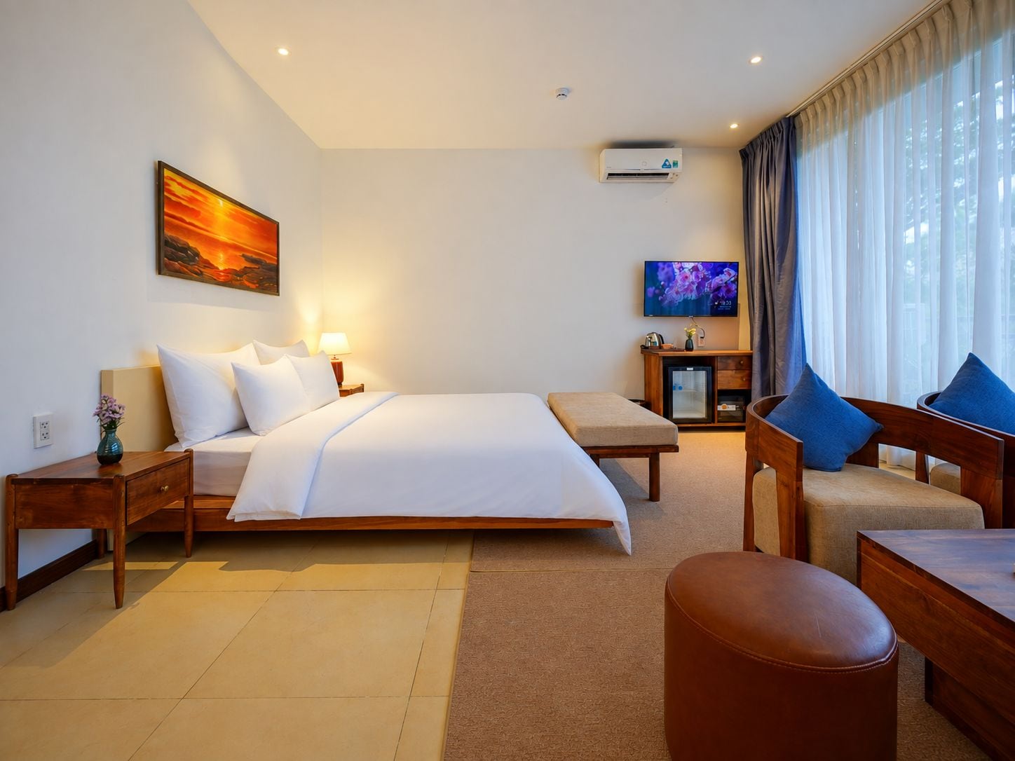 A hotel room with a bed, bedside tables, a TV, a sofa, and a window with curtains.