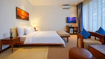 Una habitación de hotel con cama, mesitas de noche, televisor, sofá y ventana con cortinas.
