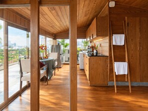 A modern kitchen with wooden cabinetry, a dining area with a table and chairs, and a view of the city through large windows. - Nexus House Lang Bao Chi (Ho Chi Minh City)