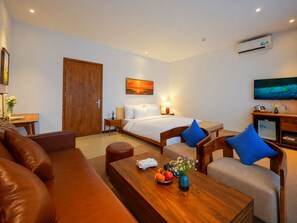 A hotel room with a bed, a sofa, a coffee table with fruit and flowers, a television, and an air conditioning unit. - Nexus House Lang Bao Chi (Ho Chi Minh City)