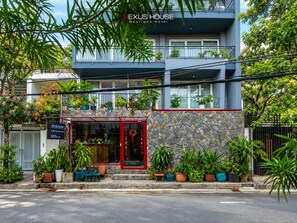 Een modern boetiekhotel met twee verdiepingen, een gevel van natuursteen, meerdere balkons en diverse potplanten.