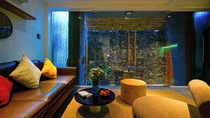 Una sala de estar moderna con una pared de piedra, sofá de cuero y una mesita con un florero y fruta.