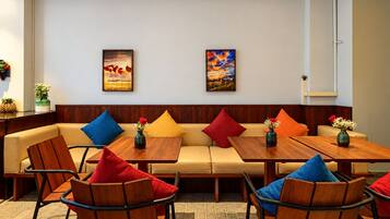 A hotel room with a sofa, two wooden tables, and four chairs.