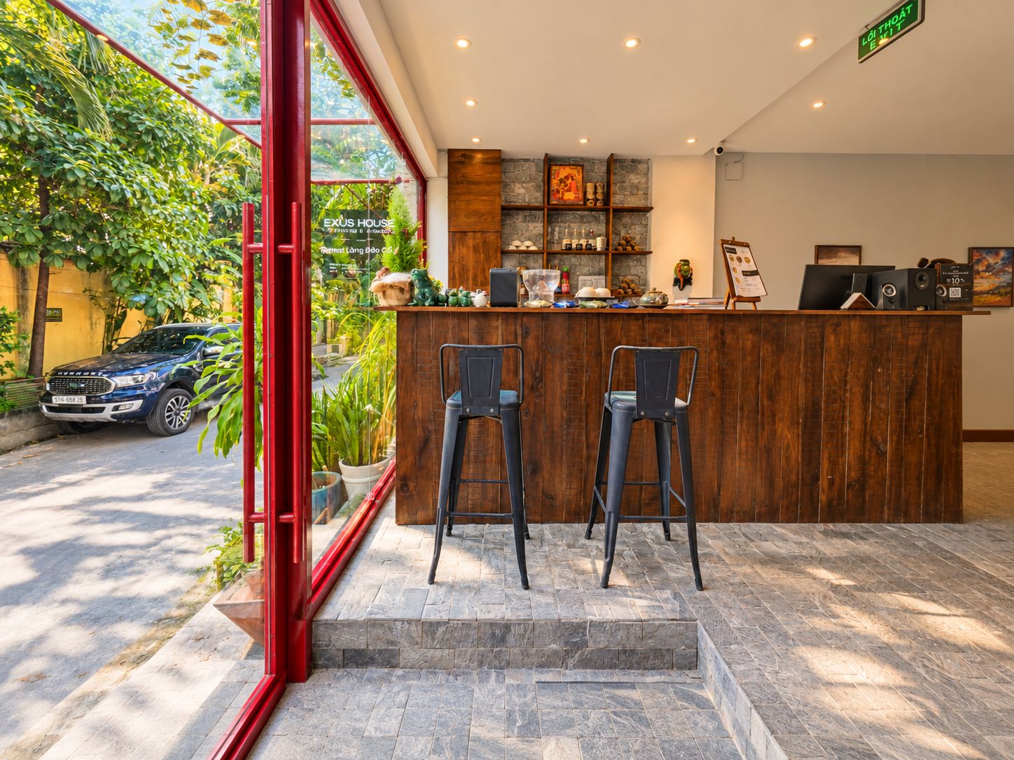 Zona de recepción con mostrador de madera, dos taburetes de bar y vista a un coche estacionado afuera.