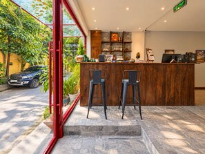 A reception area with a wooden counter, two bar stools, and a view of a parked car outside. - Nexus House Lang Bao Chi (Ho Chi Minh City)