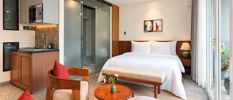 Une chambre d’hôtel comprenant un lit, un coin salon avec une table, une kitchenette et une douche.