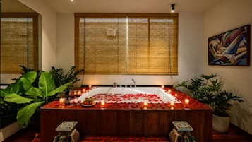 Una stanza spa con vasca, petali di rosa, candele e un quadro appeso al muro.