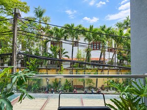 A balcony with a view of a building with palm trees and a tiled roof. - Nexus House Lang Bao Chi (Ho Chi Minh City)