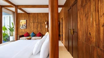 Een hotelkamer met een groot bed, houten wanden, een bank met kleurrijke kussens en een schilderij aan de muur.