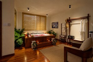 Une pièce avec une baignoire en bois, une chaise, une petite table et une grande fenêtre avec des stores en bambou.