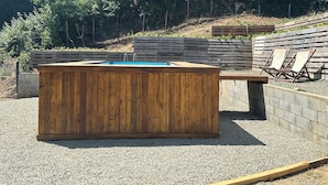 Uma banheira de madeira com interior azul, cercada por uma área de cascalho e um deck de madeira.