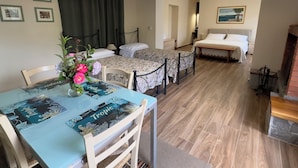 Uma área de refeições com uma mesa posta para dois, um vaso de flores e uma cama ao fundo.