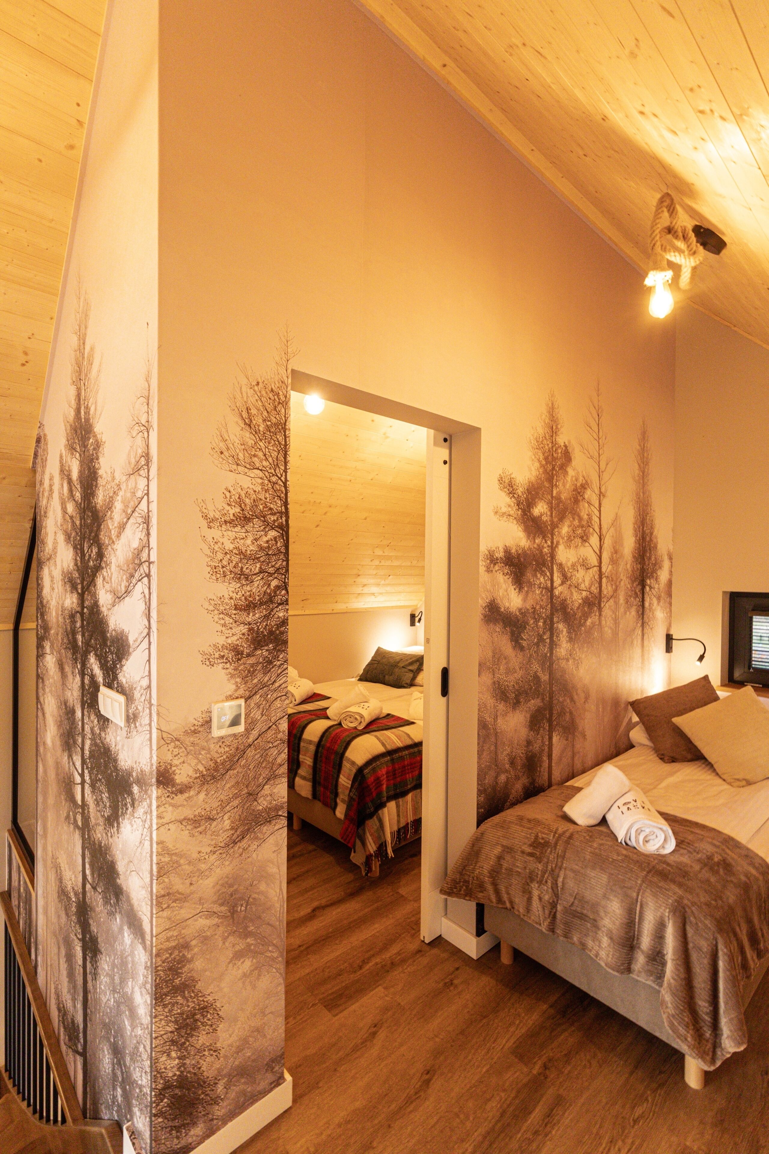 A bedroom with a bed, a nightstand, a wall-mounted TV, and a door leading to another room.