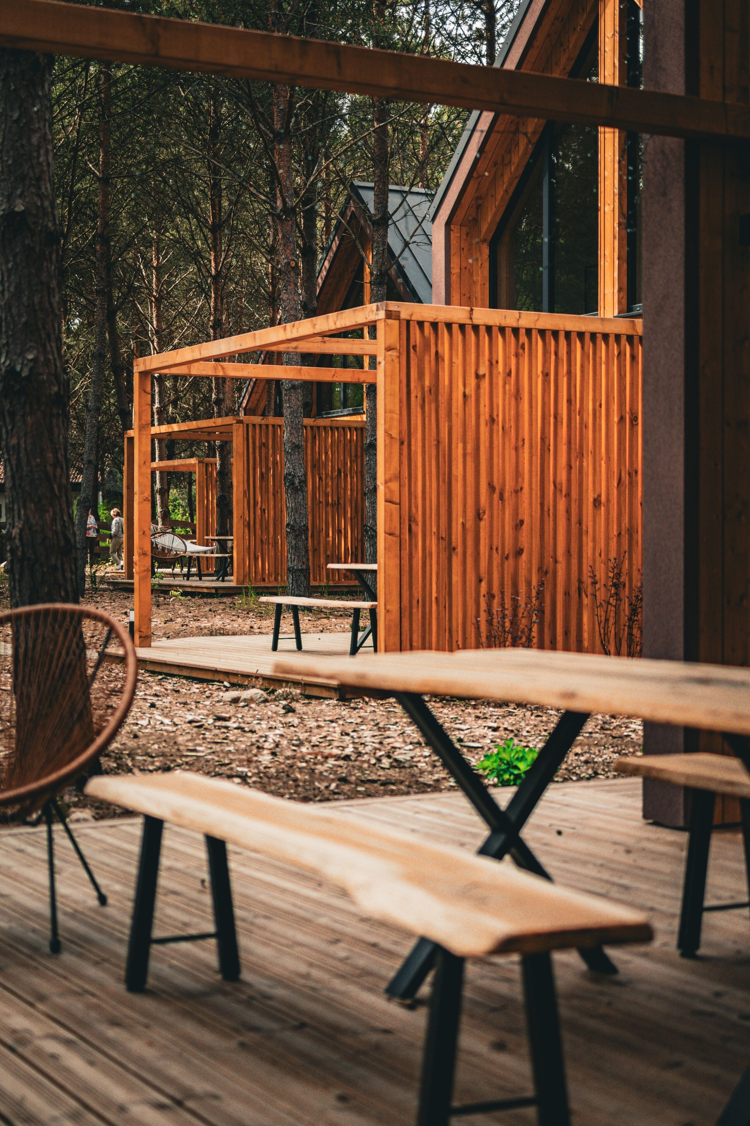 Une terrasse en bois, agrémentée de bancs et de tables de pique-nique, entourée d’arbres.