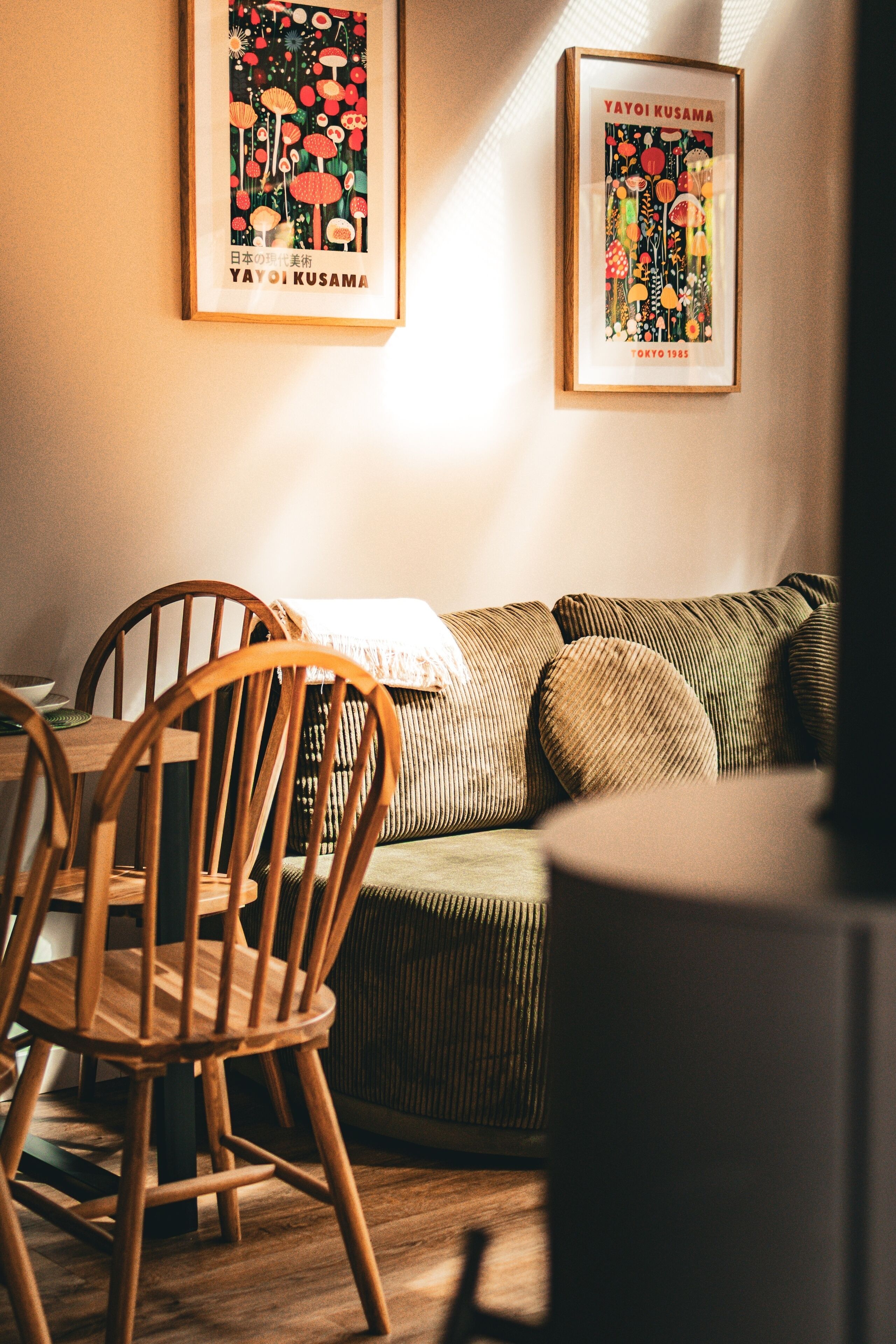 A cozy living room with a wooden dining table, a green sofa, and two framed posters on the wall.