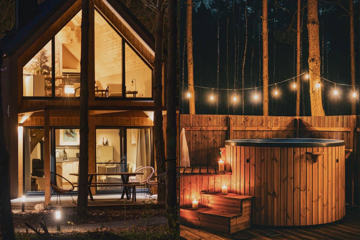A two-story wooden cabin with a hot tub and string lights, surrounded by trees.