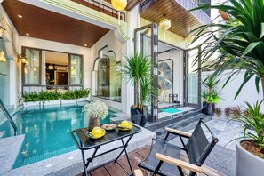 Un espace piscine intérieur moderne, doté d’une paroi vitrée, d’une table à manger avec des chaises jaunes et de plantes en pot.
