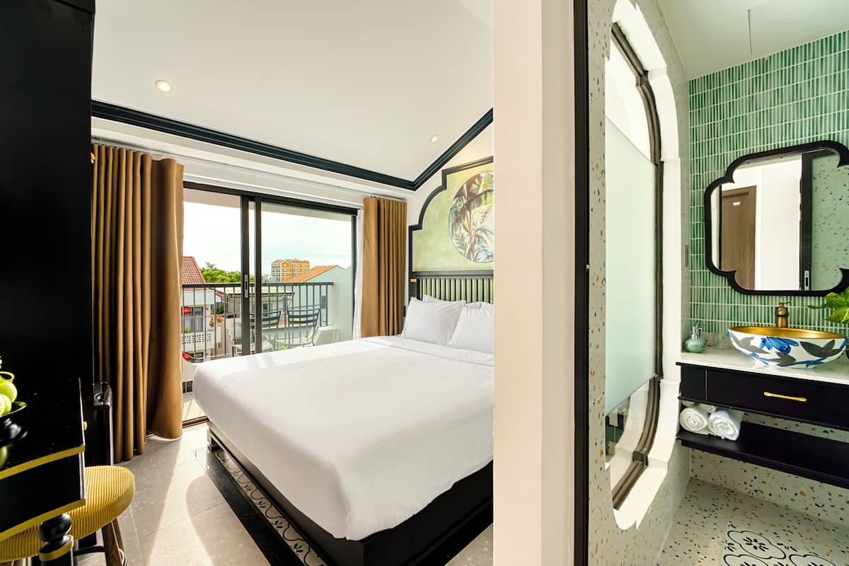 A hotel room with a large bed, a balcony with curtains, a bathroom with a large mirror and a bowl sink.