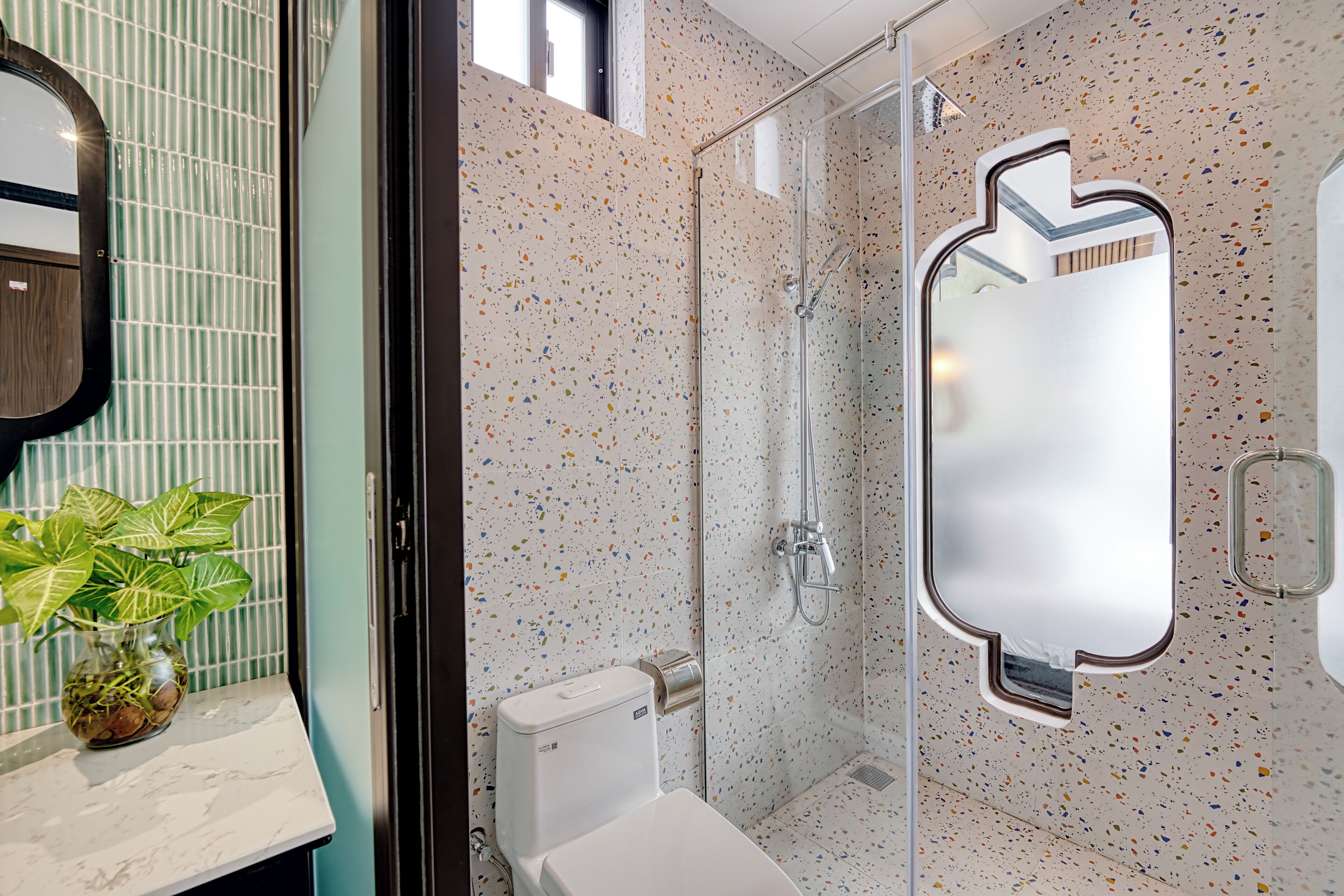 A bathroom with a glass shower enclosure, a toilet, a sink with a marble countertop, and a mirror with a unique shape.