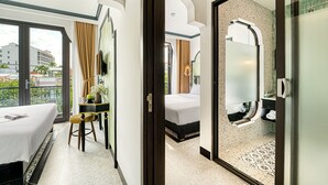 Ein Hotelzimmer mit Bett, Schreibtisch, Stuhl, Bad mit Dusche und Balkon mit Blick auf Gebäude.