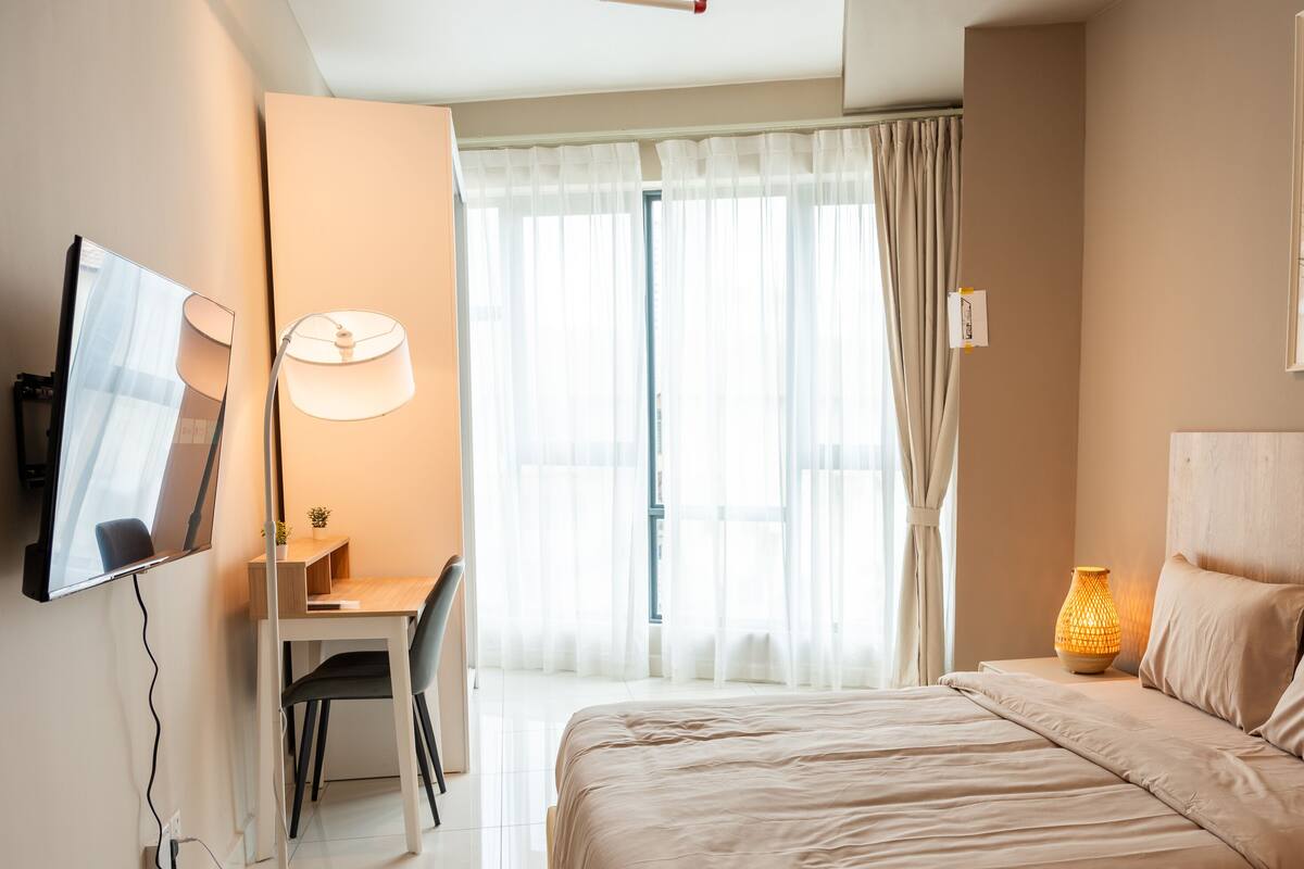 Quarto com cama, escrivaninha, cadeira, abajur e televisão.