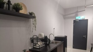 Cocina compacta con un lavamanos, una encimera con un escurreplatos y una pequeña mesa de comedor con sillas. Hay una puerta negra con un cartel encima y una planta en maceta en la pared.