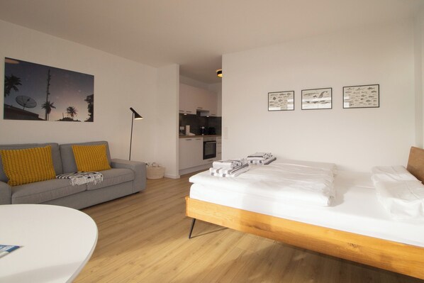 Una habitación moderna con cama, sofá, zona de comedor y cocina al fondo.