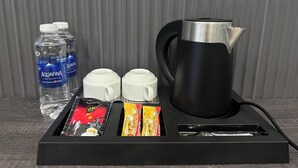 Une machine à café, deux tasses blanches, une bouteille d’eau et des en-cas sur un plateau.