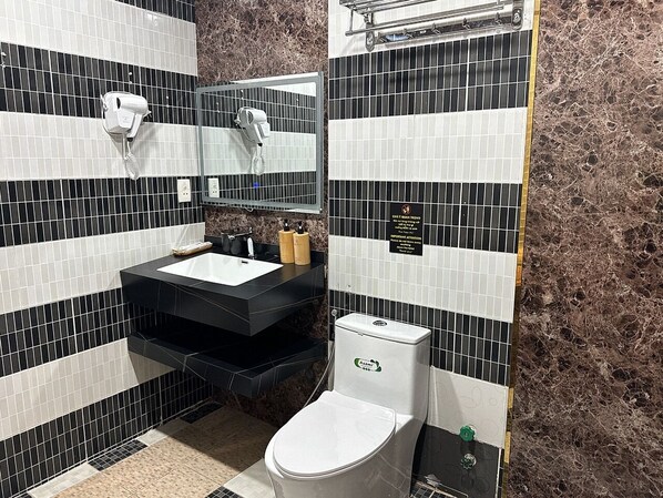 Un baño con salpicadero blanco y negro, un lavabo con encimera negra, un inodoro blanco y un espejo sobre el lavabo.