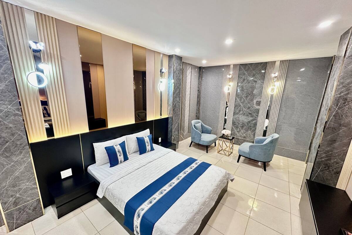 A modern bedroom with a large bed, two armchairs, and a mirror.