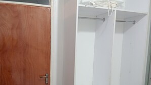 Una habitación con puerta de madera, un armario blanco con estantes y suelo de baldosas.
