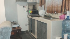 Cocina compacta con microondas, lavamanos y dispensador de agua. Incluye una pequeña mesa de madera y una silla.