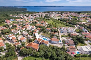 An aerial view of a coastal residential area with houses, a swimming pool, and a clear view of the sea. - Mery's Sunny Pool Apartment (Vodnjan)