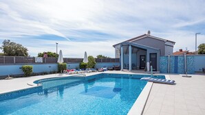 Ein Schwimmbecken mit Liegestühlen und Sonnenschirmen, eine überdachte Sitzgelegenheit und eine geflieste Terrasse.