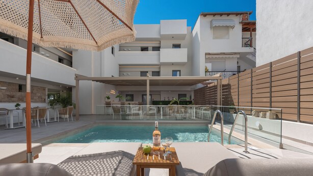 A poolside area with a table, chairs, and a bottle of wine. - Sandy Seaside Suites (Nea Propontida)