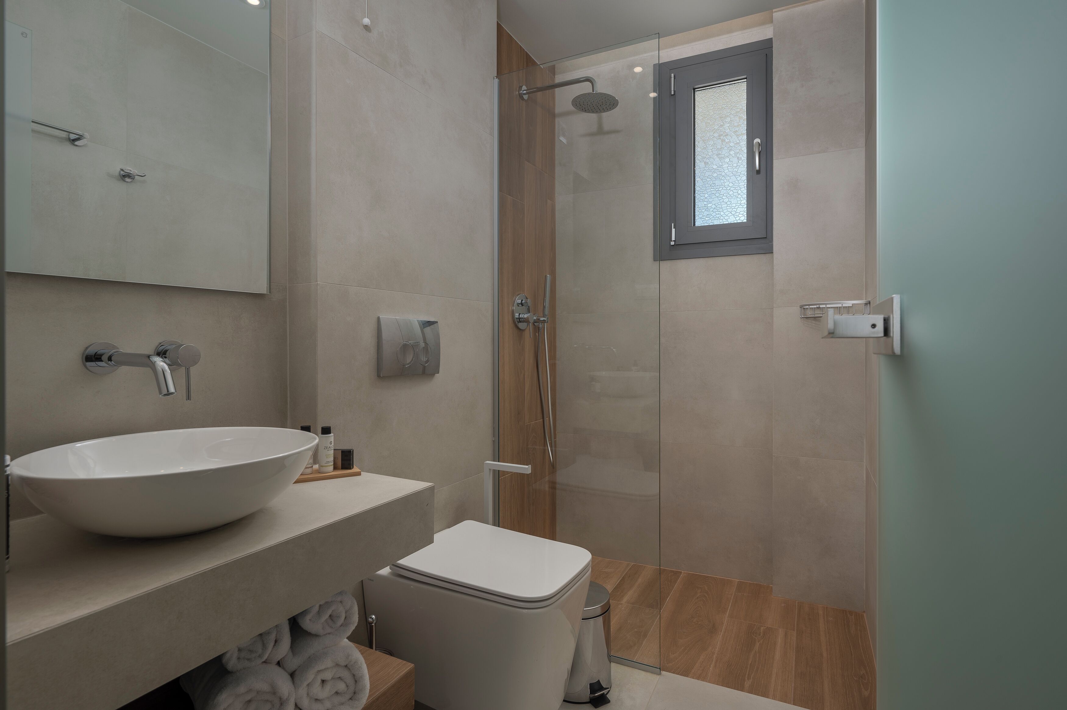 Un baño moderno con un lavamanos blanco grande, un inodoro y una zona de ducha con mampara de vidrio.