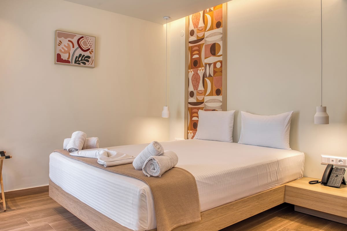 A modern hotel room with a large bed, a bedside table with a phone, and a wall art piece.