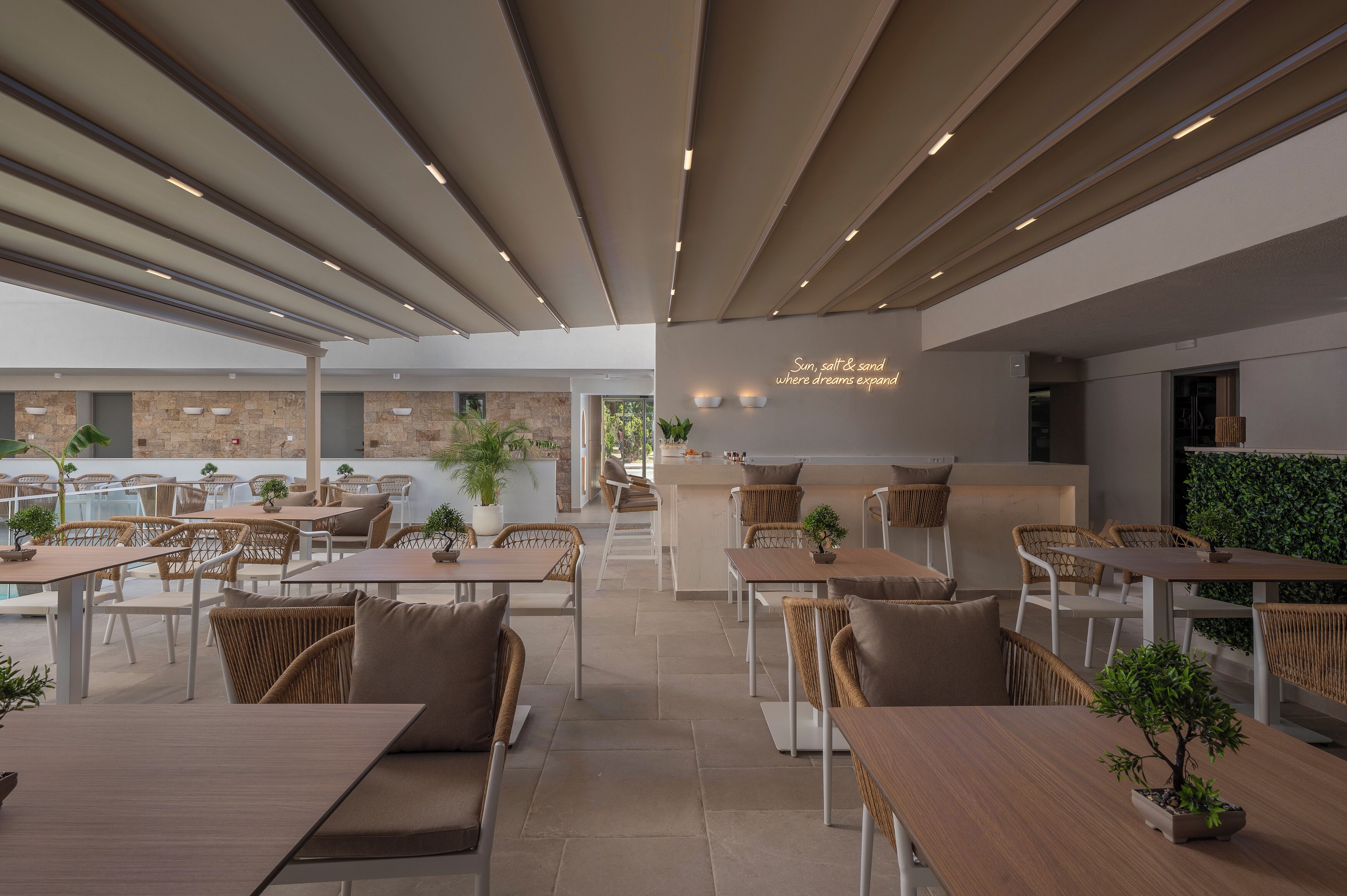 A modern outdoor dining area with multiple tables and chairs, a bar area, and a view of the surrounding landscape.